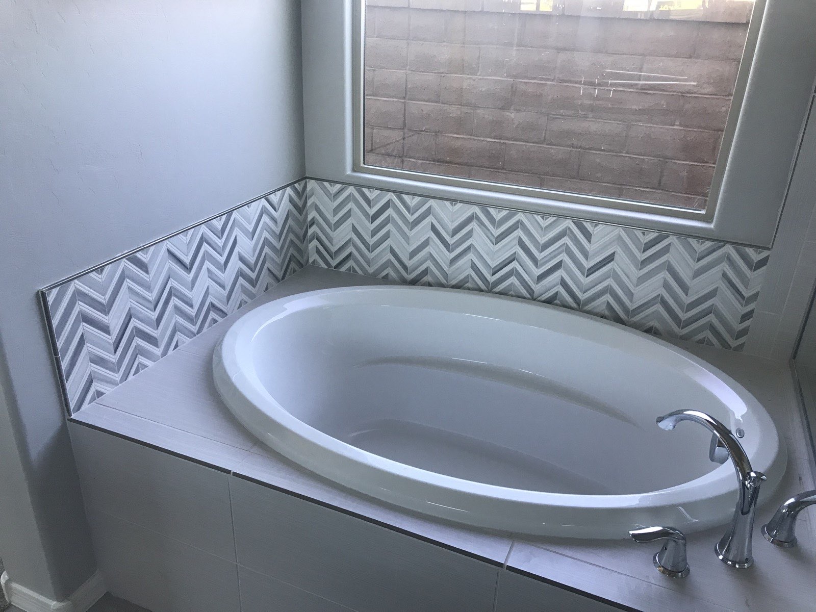 Built-in oval tub with chevron mosaic tile surround and chrome fixtures