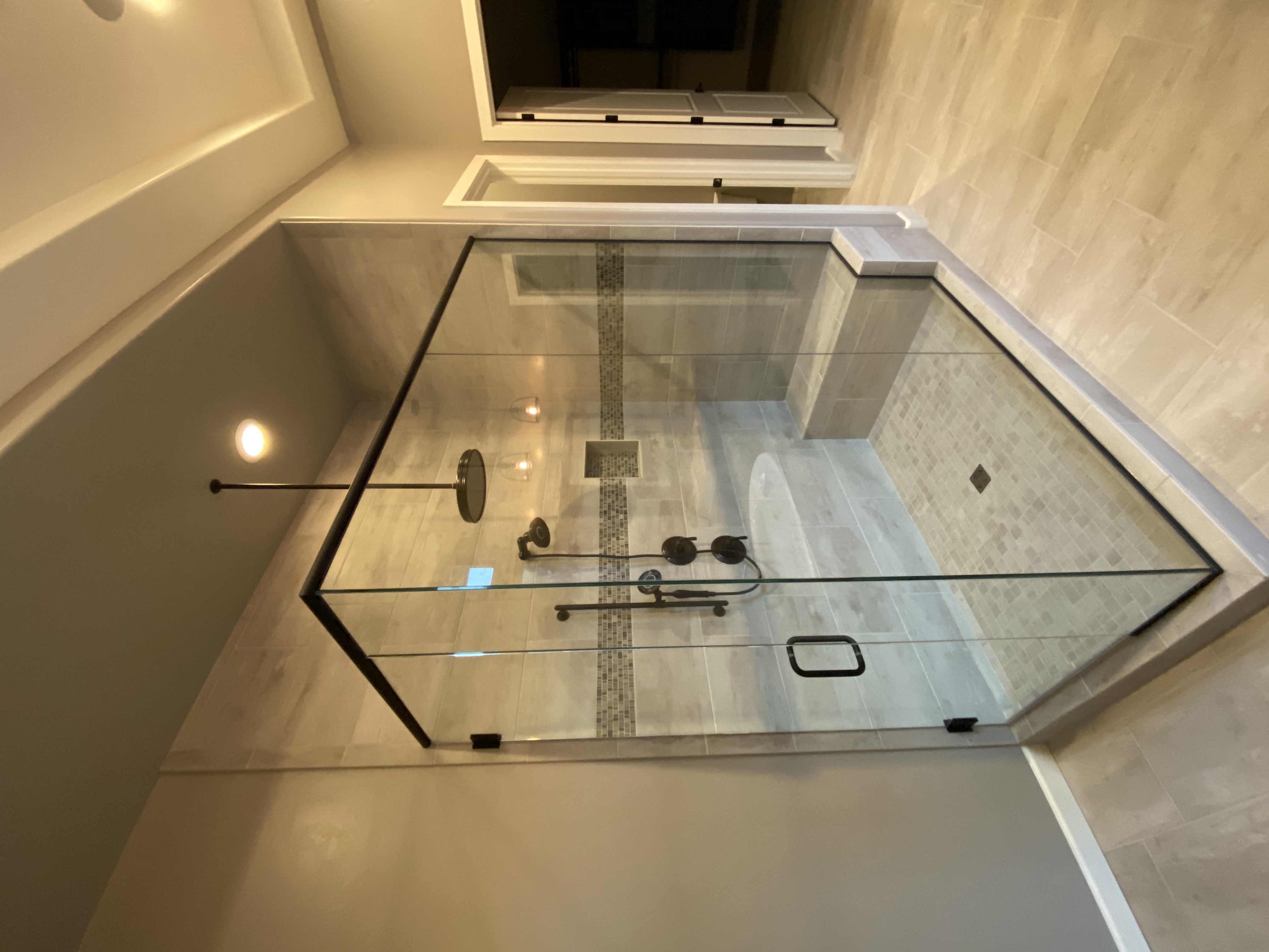 Walk-in shower with marble-look wall tile, mosaic floor, and glass partition