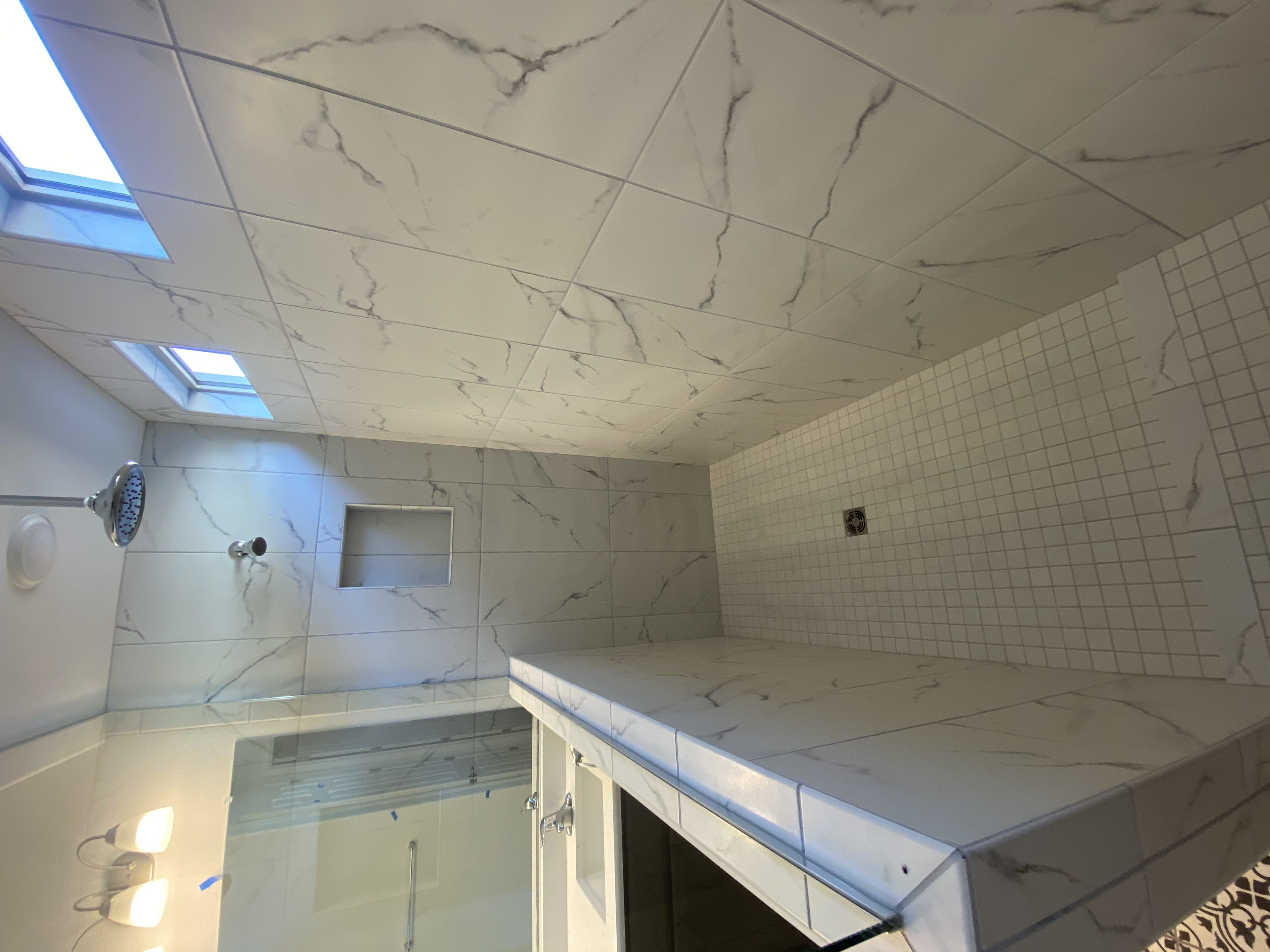 Walk-in shower with marble-look tile, dark accent band, mosaic floor, and bench