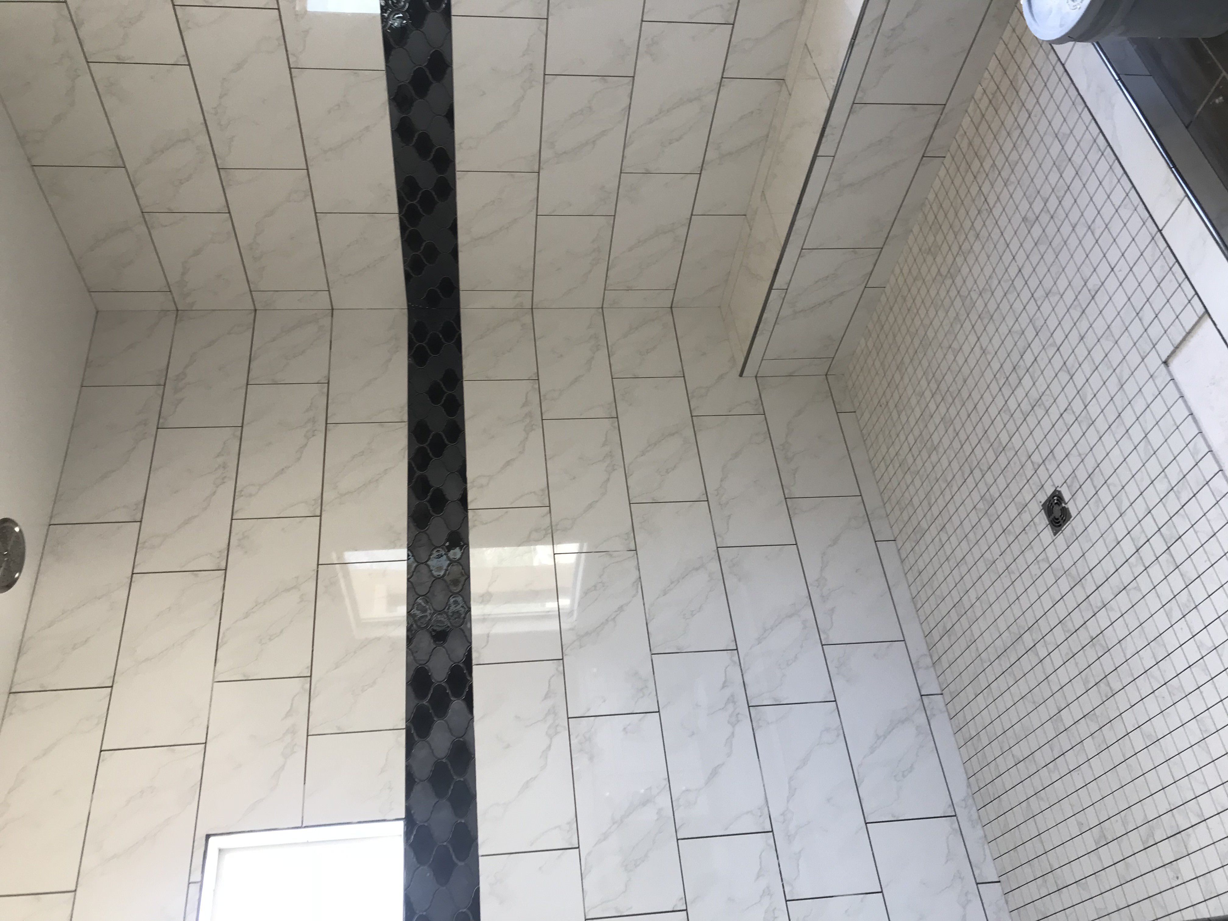 Frameless glass shower with textured white wall tile, dark mosaic floor, and black fixtures