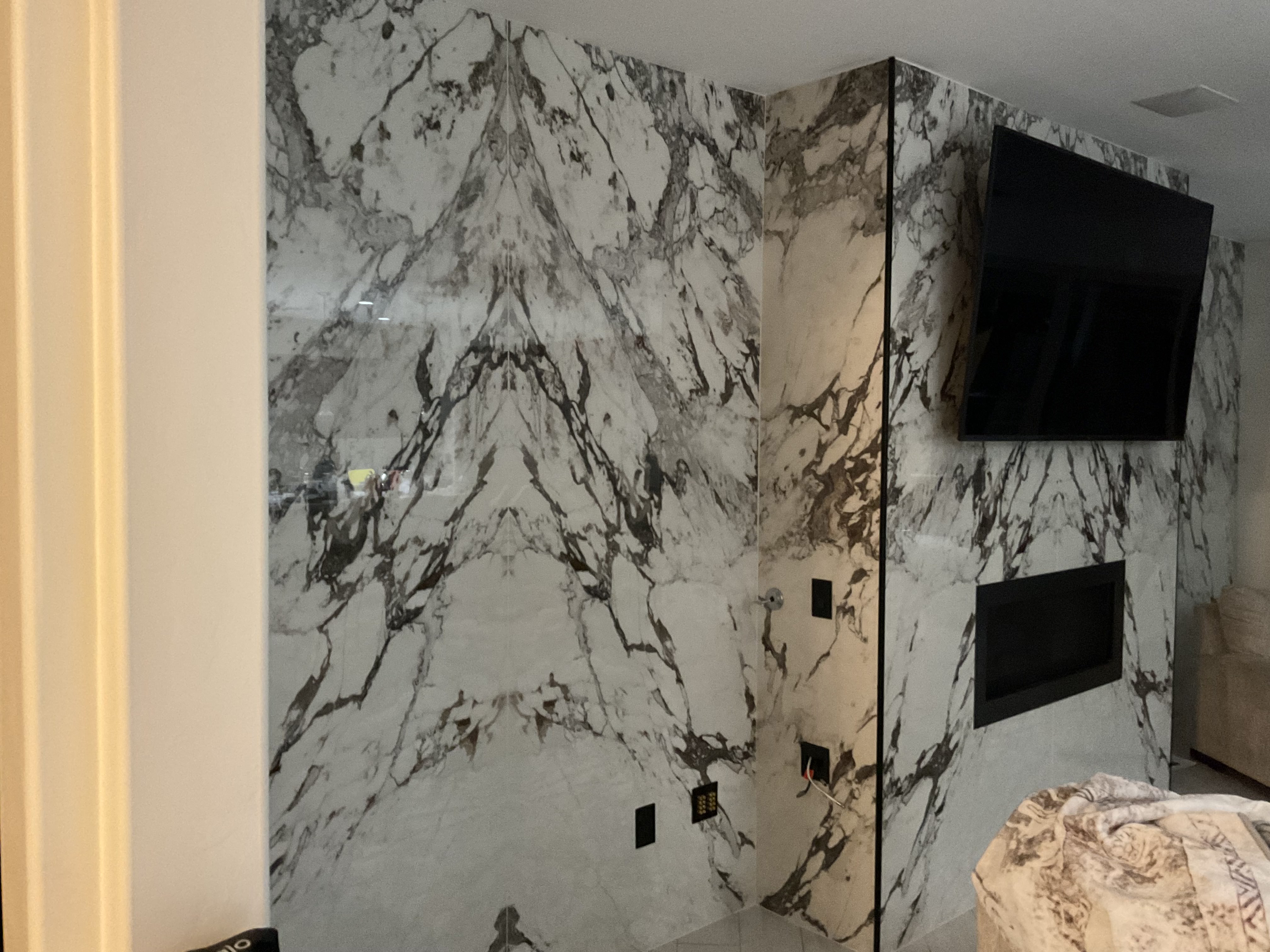 Floor-to-ceiling book-matched marble-look wall with linear fireplace and TV